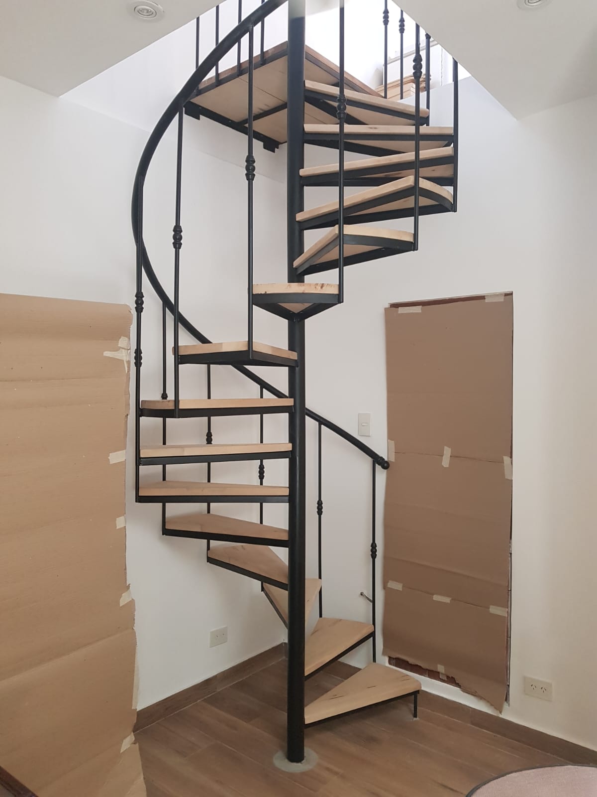 Escalera caracol de hierro forjado con peldaños de madera clara, obra en proceso