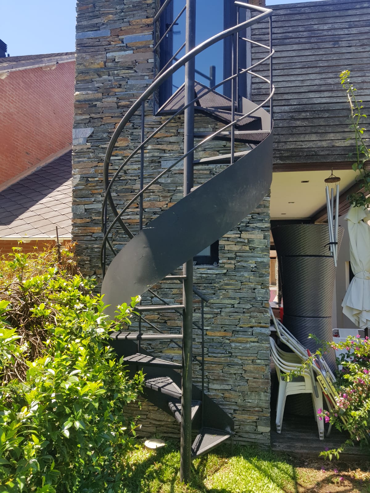 Escalera caracol color antracita exterior junto a pared de piedra