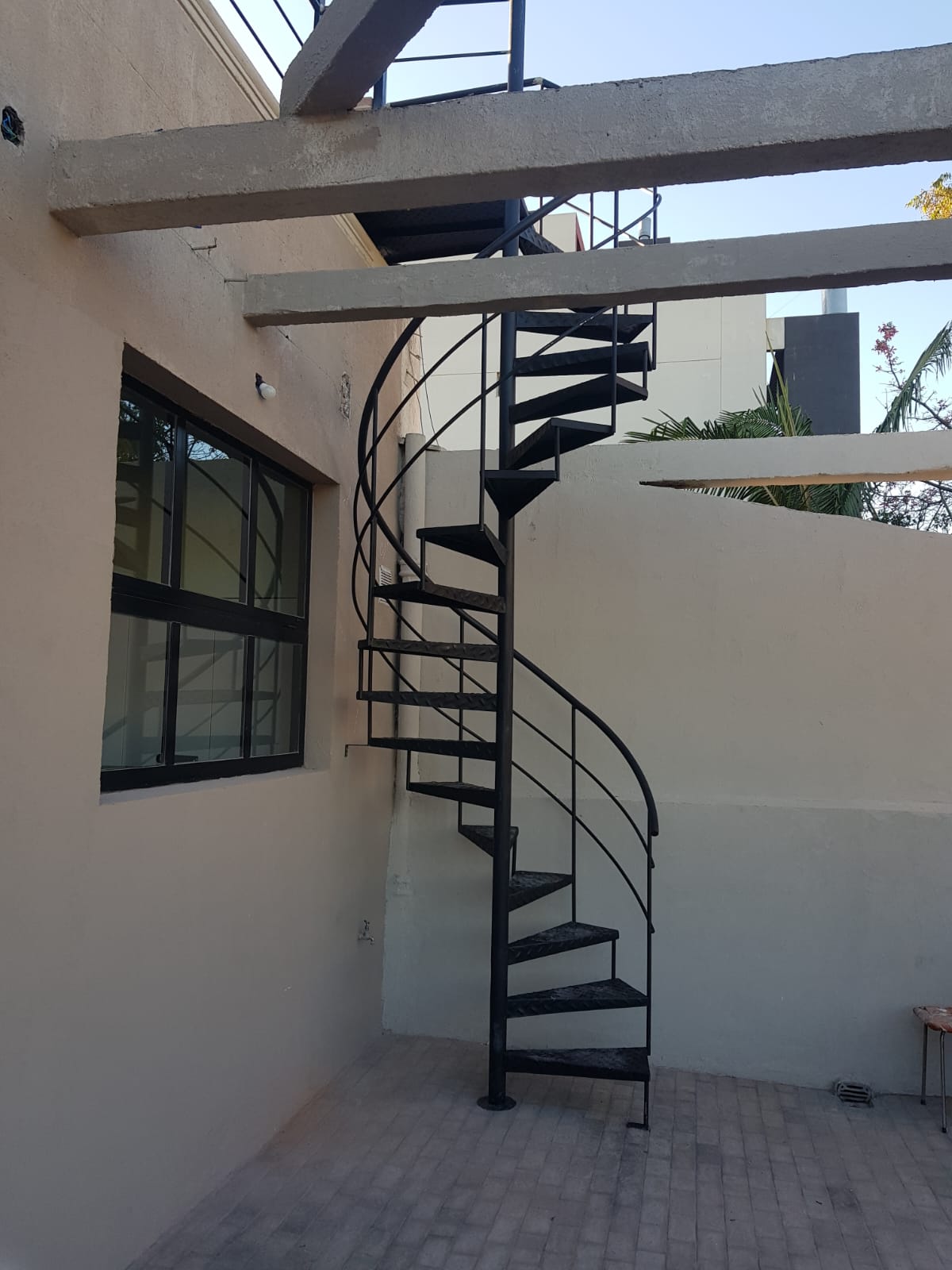 Escalera caracol negra exterior entre vigas de hormigón
