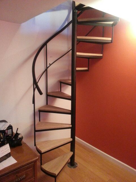 Escalera caracol con peldaños de madera clara, interior junto a pared naranja
