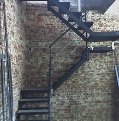Escalera recta negra interior en obra, pared de ladrillo visto