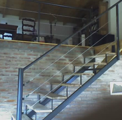 Escalera recta negra interior con baranda de cable, entrepiso de ladrillo visto