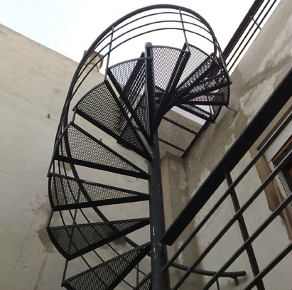Escalera caracol negra exterior con peldaños de rejilla, vista desde abajo