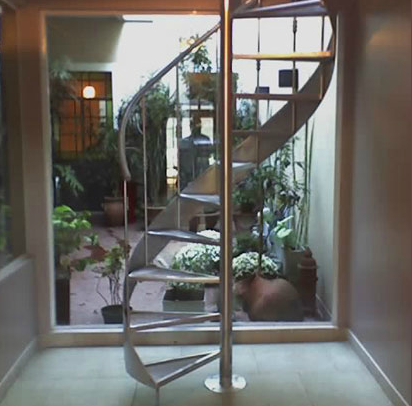 Escalera caracol de acero inoxidable en patio interno con plantas
