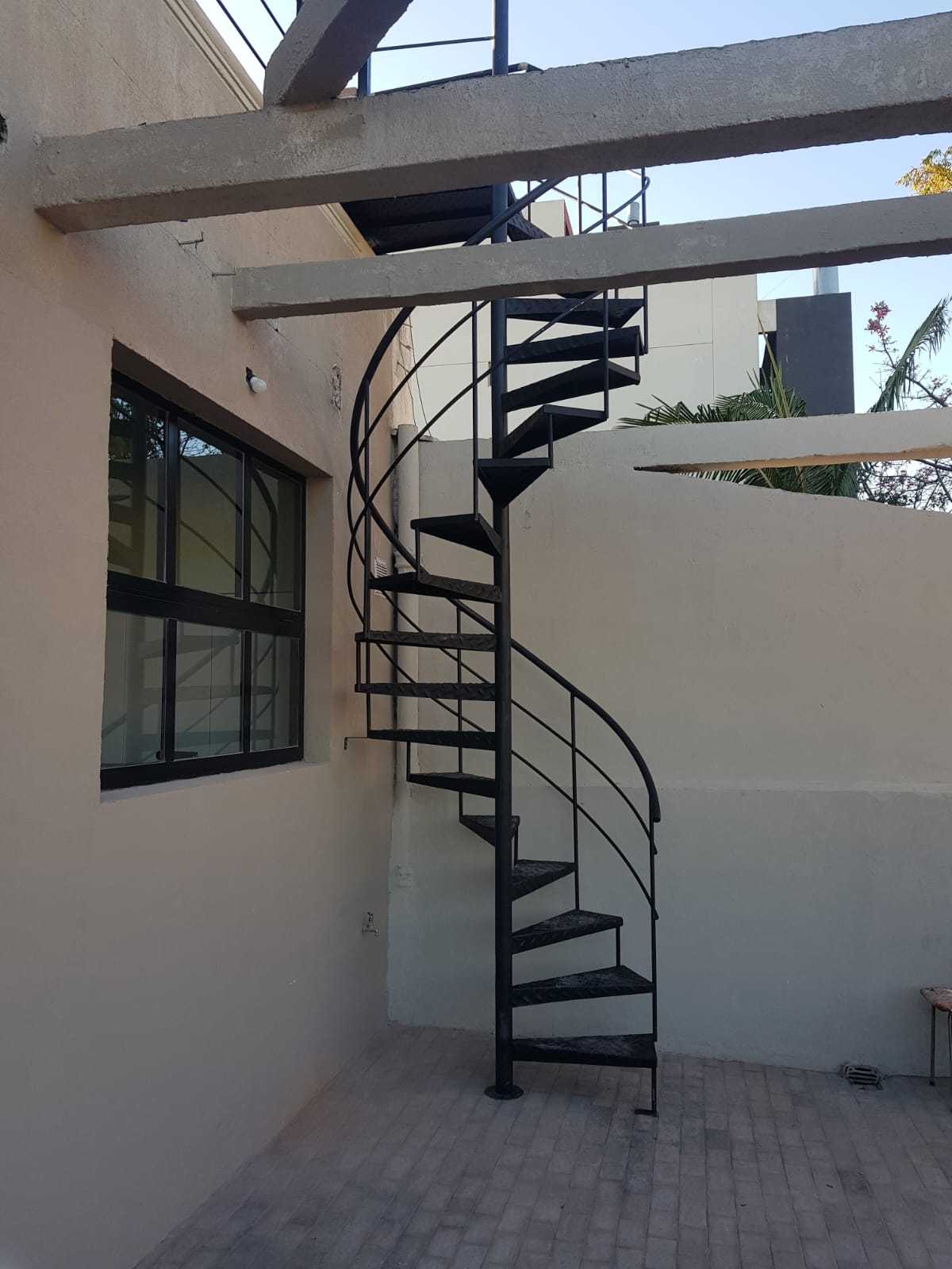 Escalera caracol negra exterior bajo vigas de hormigón, en terraza