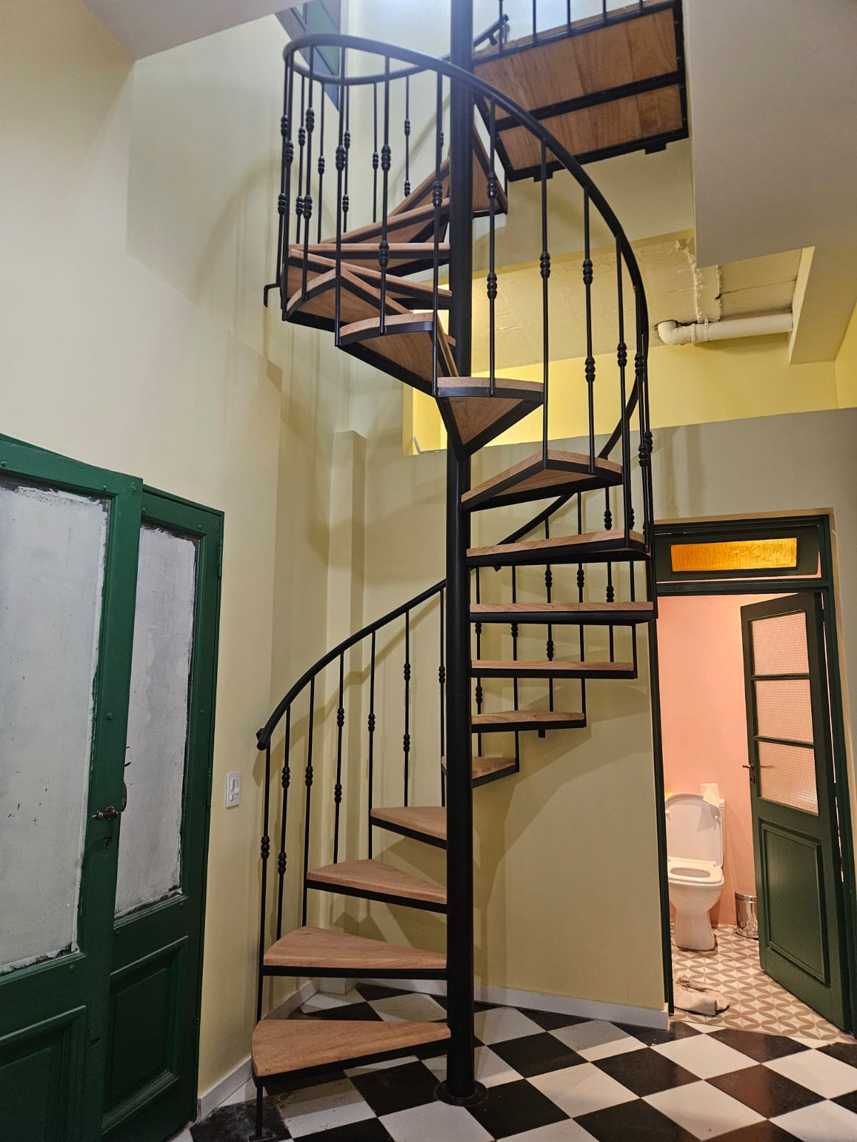 Escalera caracol de hierro forjado fabricada por Escafull, instalada en interior con piso damero