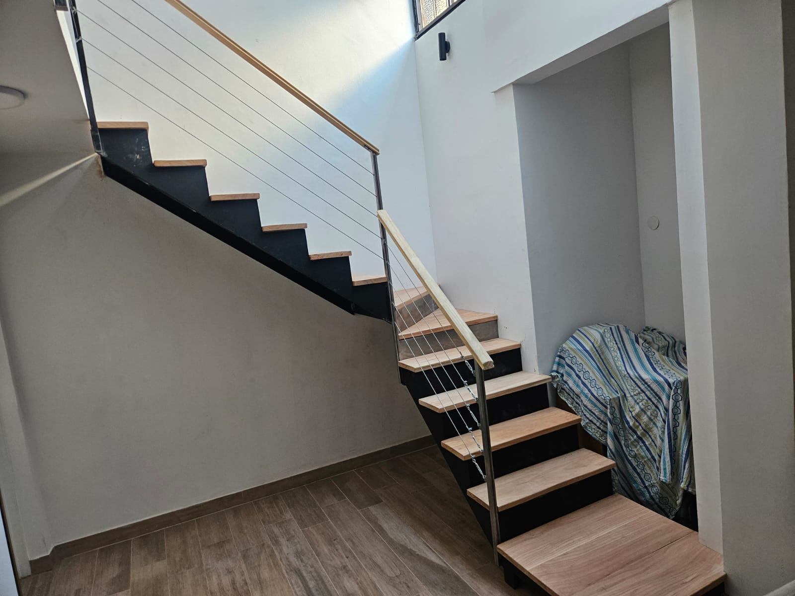 Escalera recta interior con estructura de hierro, peldaños de madera y baranda de cables