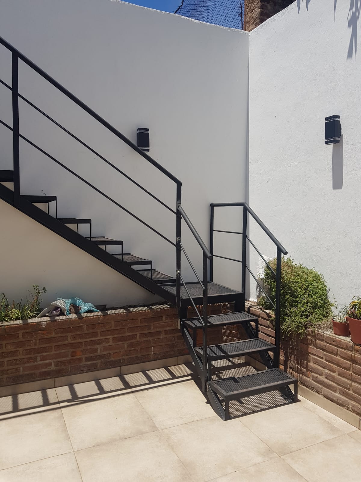 Escalera recta negra exterior junto a macetero de ladrillo