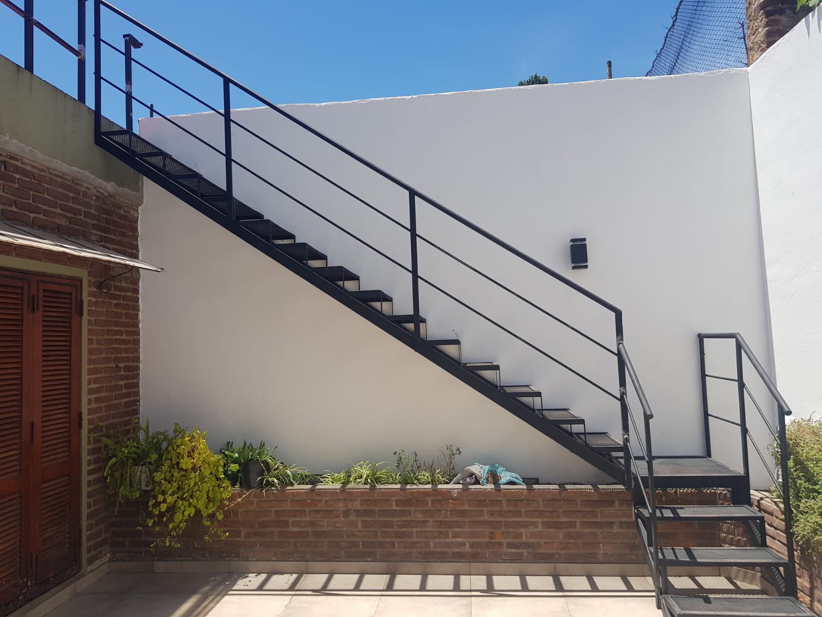 Escalera recta negra exterior junto a macetero de ladrillo, vista lateral
